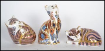 A group of three royal crown derby china cat paperweights to include two one Imari style paperweight