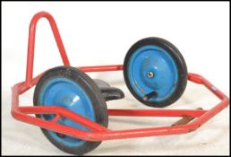 A vintage retro 20th century hand crank pedal bike of red tubular construction with blue wheels.