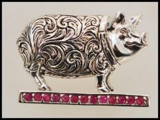 A stamped sterling silver brooch in the form of a pig with engraved folate decoration, set with