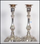 A pair of silver candlesticks raised on stepped square bases with scrolls with bulbous stem and