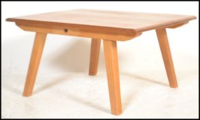 A beech and elm low coffee table having a plank top raised on angled tapering legs. The table up-