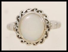 A 14ct white gold opal ring having a central opal panel in scrolled mount. Stamped 14k and tests