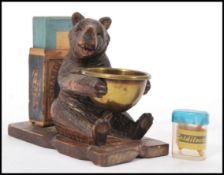A mid 20th Century carved pine black forrest match striker in the form of a bear holding a brass