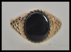 A hallmarked 9ct gold signet ring set with an oval black stone and pierced decoration to the