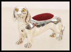 A silver pincushion in the form of a daschund dog having yellow and black glass eyes and a red