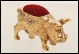 A copper pincushion in the form of a pig with engraved detailing having a red fabric cushion to