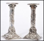 A pair of Chinese silver white metal candlesticks raised on square bases with cylindrical columns