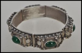 A decorative large silver bracelet with 6 individual bars adorned with cabochon green stones to