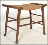 An early 20th century Arts and Crafts style squat stool raised on tapering wooden legs with rattan