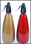 Two retro  20th century soda siphons having red and gold bodies with black and chrome tops.