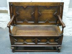 A carved oak monk's bench with shaped fluted arms,