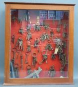 A mahogany display cabinet containing antique and vintage keys, bird or duck call, corkscrews etc,