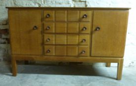 Gordon Russell light oak sideboard with two doors either side of four straight drawers raised on