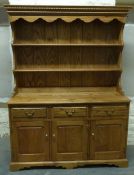 An elm dresser with three drawers over cupboards with plate rack above and brass handles,