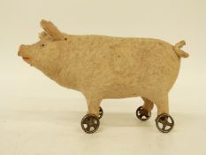 A late 19thC/early 20thC felt covered pig on wheels with squeak, glass eyes and composite snout,