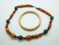 An amber necklace with white metal filigree fittings (61g) & a carved ivory bangle