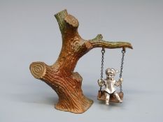 A novelty white metal and cold painted bronze girl on a swing,