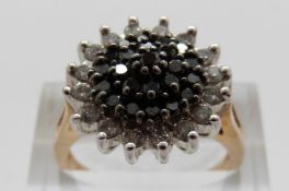 A 9ct gold ring set with black diamonds surrounded by a border of clear diamonds in a large cluster,