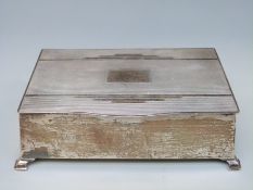 An Art Deco hallmarked silver cigarette box with engine turned decoration, raised on four feet,