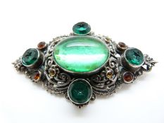 A silver brooch set with a large foiled green cabochon and further green paste and orange paste
