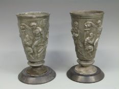 A pair of pewter vases depicting mythical figures, on slate bases,