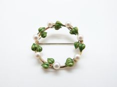A yellow metal brooch set with green enamel and pearls in a circular floral design