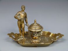 A brass inkwell decorated with a jockey or similar figure,