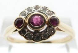 A 14ct gold ring set with three central rubies in an oval diamond surround,