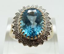 A 9ct gold cocktail ring set with an oval cut blue topaz with diamond surround, size U/V, 4.
