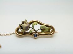A 9ct gold Art Nouveau brooch in the form of a flower set with enamel, seed pearls and a sapphire,