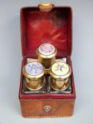 A late 19thC or early 20thC leather cased travelling set containing three glass bottles with floral