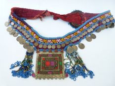 An Eastern beaded ceremonial belt decorated with coins bearing Arabic script and a foiled glass