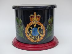 A hand painted cylindrical wooden box / stool with lid, decorated with old GCHQ logo.