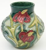 Moorcroft squat vase decorated with red flowers on a green ground,