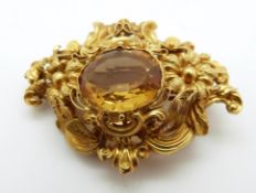 A yellow metal Victorian brooch set with an oval cut citrine in floral and foliate border