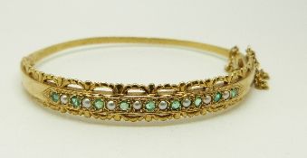 A 9ct gold bangle set with seed pearls and alternating emeralds