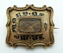 A Georgian brooch set with plaited hair surrounded by black enamel writing 