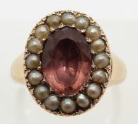 A Victorian ring set with an oval pink sapphire surrounded by seed pearls in a closed back setting,