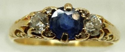 A Victorian 18ct gold ring set with a central sapphire and two diamonds in a scrolling setting,