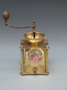 A brass coffee grinder with inset ceramic plaque, embossed decoration and turned wooden handle,