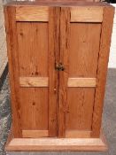 A pine cupboard with panelled doors and three shelves within,