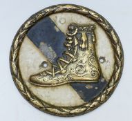 A 19thC brass plaque with relief moulded shoe or boot in laurel leaf surround,