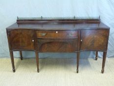 A 19thC James Shoolbred serpentine fronted mahogany sideboard raised on eight tapering legs with