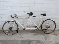 A vintage tandem bicycle with white frame and drum brakes