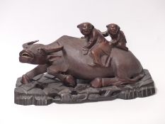 Chinese carved wooden water buffalo with figures on its back and bone teeth, on hardwood stand,