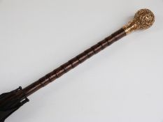 A late 19thC/20thC parasol with spherical yellow metal repoussé decorated handle with cane stick,