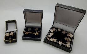 A silver necklace made up of leaf links with matching earrings and a pair of silver earrings in the