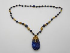 A large carved lapis lazuli drop pendant with serpent and pharaoh decoration on a beaded necklace