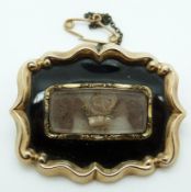Victorian gold mourning brooch set with black enamel scrolling borders and a glass compartment to
