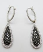 A pair of 14ct white gold earrings set with black diamonds and diamonds in a pear shaped drop,